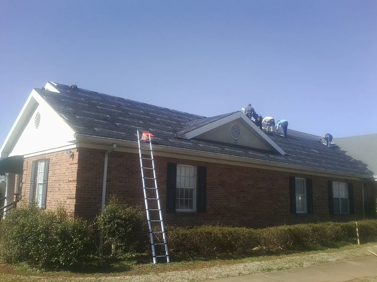 Crew tearing shingles off a brick ranch roof with a ladder set — Emergency Roof Repair work by our crew in Danvers