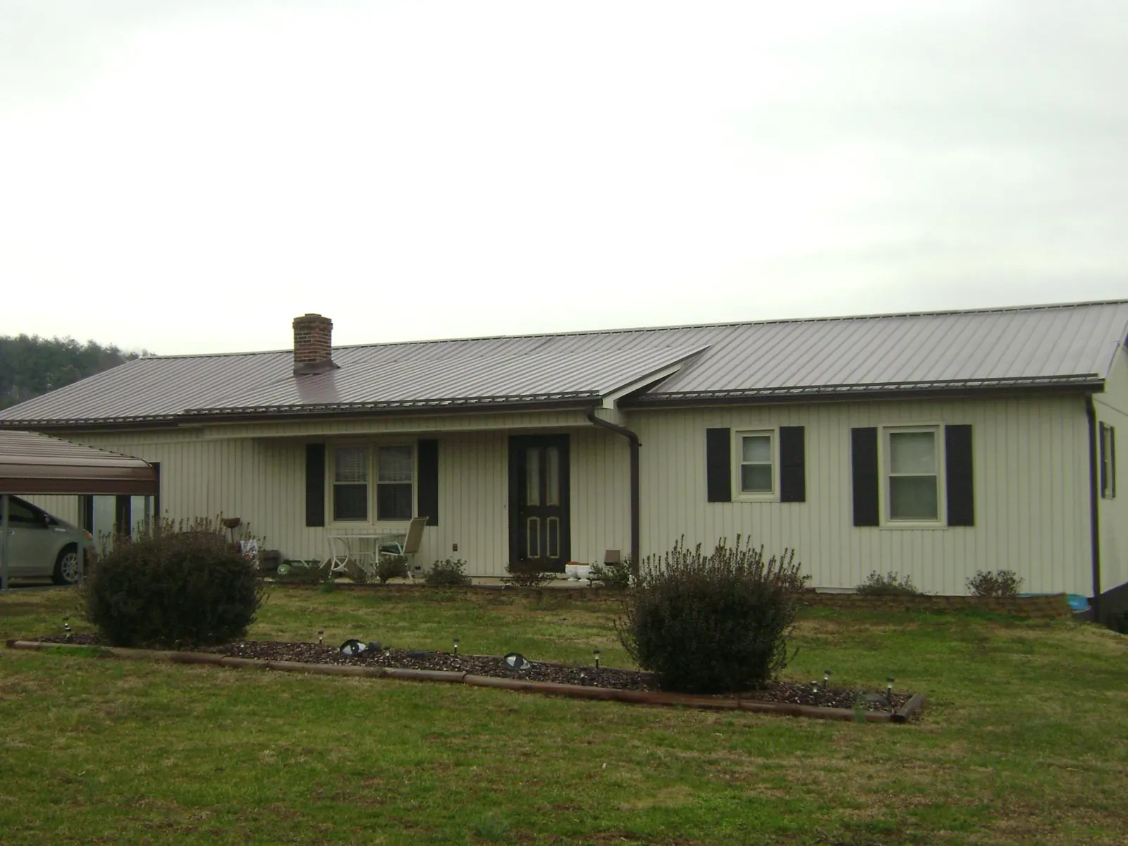 Brown metal roof on a cream sided ranch home with a brick chimney in Danvers